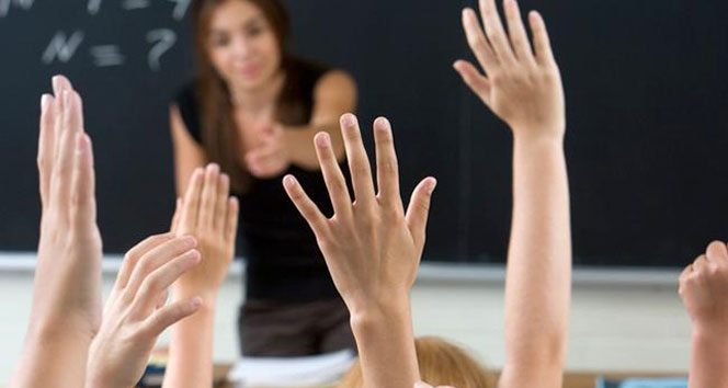Siyah giyinimli bir kadın öğretmen elini öğrencilere doğru uzatıyor. Öğrenciler ise ellerini havaya kaldırmış şekilde söz istiyor