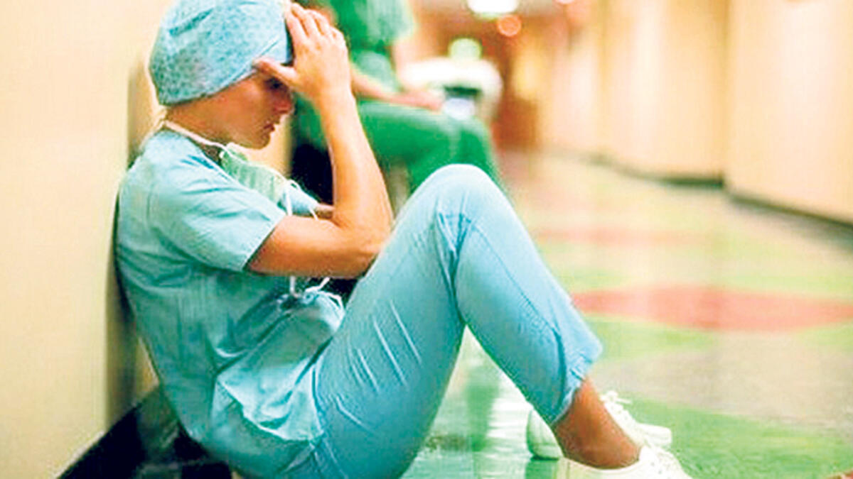 Bir sağlık çalışanı yerde oturmuş, ellerini başına dayamış şekilde görülüyor.
