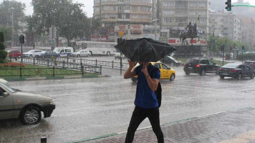 Sağanak bir şekilde yağan yağmur altında erkek bir kişi şemsiyesini açarak yürüyor. Hemen yan tarafından araçlar trafikte ilerliyor