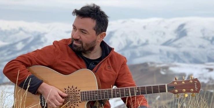 Apolas Lermi elinde gitarıyla karlı bir dağın önünde oturuyor