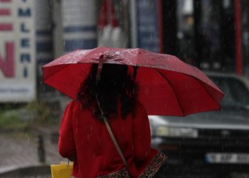 Kırmızı şemsiye taşıyan bir kadın yolda yürüyor