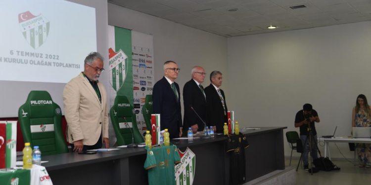 Dört kişi bir masanın arkasında ayakta duruyor. Önlerinde Yeşil beyaz renkli Bursaspor forması asılı