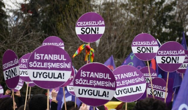 Birileri tarafından havaya tutulan karton mor dövizler var. Dövizlerin üzerinde "İstanbul Sözleşmesi'ni uygula" ve "Cezasızlığa son" yazıyor