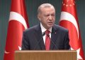 Cumhurbaşkanı Recep Tayyip Erdoğan, kürsüde konuşma yapıyor. Erdoğan'ın arkasında iki tane Türkiye Cumhuriyeti bayrağı var, birinin üzerinde Cumhurbaşkanlığı forsu görülüyor