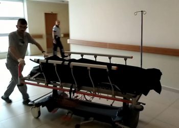 Siyah bir örtüyle üzeri kapatılmış genci bir hastane personeli sedyede taşıyor.