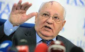 Gorbaçov sağ elini havaya kaldırmış, önünde mikrofonlar açıklama yapıyor.
