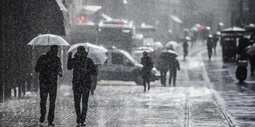 Yağmur altında insanlar şemsiyeleriyle caddede yürüyor