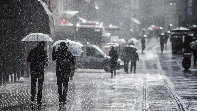 Yağmur altında insanlar şemsiyeleriyle caddede yürüyor