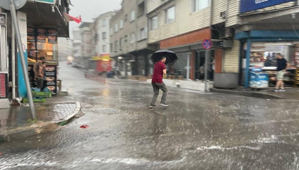 Bir yurttaş elindeki şemsiyeyi zor tutar vaziyette su akan yoldan geçmeye çalışıyor
