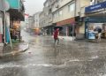 Bir yurttaş elindeki şemsiyeyi zor tutar vaziyette su akan yoldan geçmeye çalışıyor