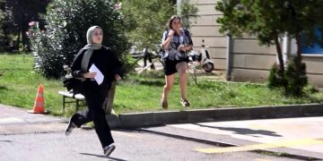 İki kadın öğrenci birinin elinde sınav giriş kağıdıya birlikte koşuyor