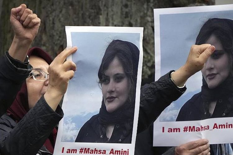 Siyah başörtülü kadınlar ellerinde "ı am #Mahsa Amini" yazılı görsellerle Mahsa Amini'nin fotoğrafını taşıyor"