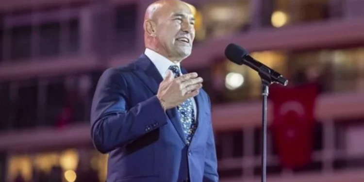 İzmir Büyükşehir Belediye Başkanı Tunç Soyer, konser için kurulan platformda bir elini göğüs hizasına getirerek önündeki ayaklı mikrofon aracılığı ile İzmirlilere sesleniyor.
