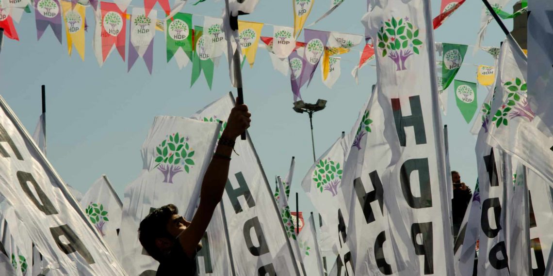 HDP bayraklarının yer aldığı bir alanda bir kişi elindeki HDP bayrağını havaya kaldırıyor.