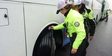 İki trafik polisi durdurdukları otobüsün tekerlerini kontrol ediyor.