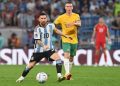 Arjantinli futbolcu Messi ve Avustralyalı futbolcunun önünde topa vuruyor.