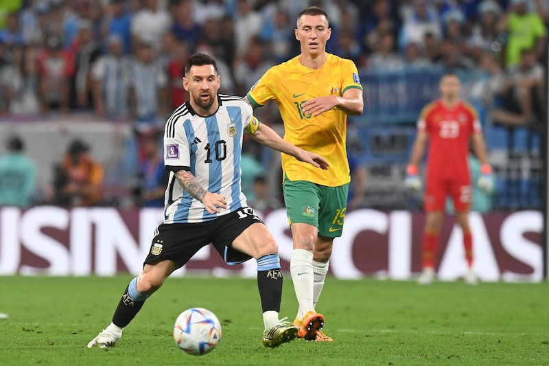 Arjantinli futbolcu Messi ve Avustralyalı futbolcunun önünde topa vuruyor.