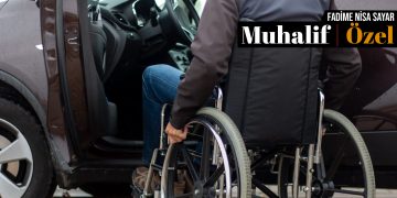 Bir otomobilin sürücü koltuğunun yanında tekerlekli sandalyede biri oturuyor.