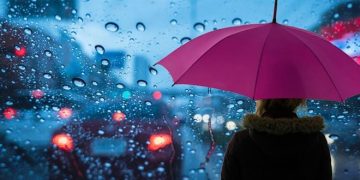 Yağmurlu bir havada mor şemsiyeli bir kadın bekliyor.